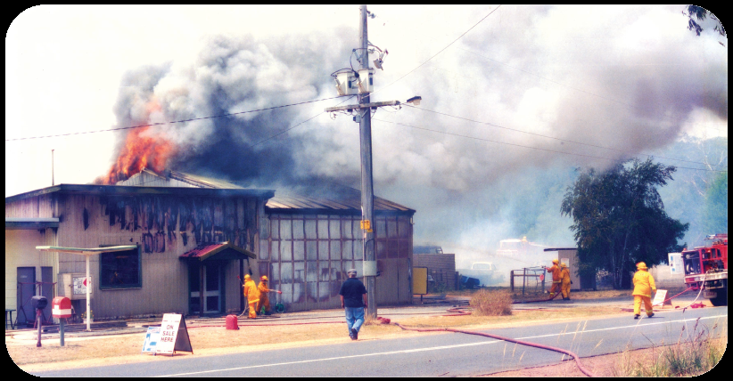 Dereel general store with fire and smoke billowing from roof and firefighters attempting to extinguish